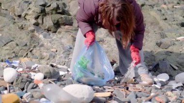 Doğada bırakılan çöpler kirlilik nedeniyle çevresel hasara yol açar. Eldivenli bir kadın yerden çöp ve plastik atık temizliyor. 