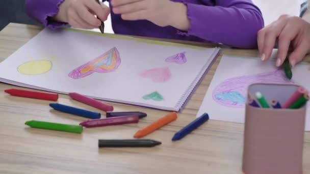 異なる色の鉛筆とクレヨンを使用してテーブルの上に彼女の母親と一緒に小さな女の子の絵の肖像画を閉じます笑顔楽しい学習図面を持っています — ストック動画
