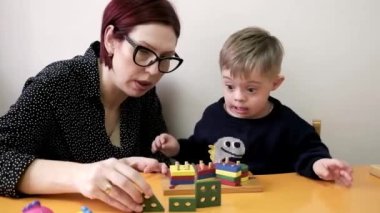Özel ihtiyaçları olan sevimli çocuk kreş merkezindeki oyuncaklarla oynuyor. Öğretmen ona eğitim oyunları oynaması için yardım ediyor..