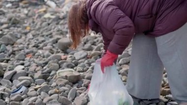 Kırmızı lastik eldivenli, çöp torbalı, plastik şişe ve diğer atık parçaları toplayan, parkı veya plajı temizleyen gönüllü.