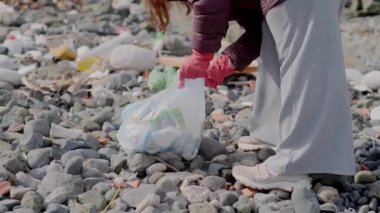 Yakın planda, bir gönüllü sahilde çöp topluyor, Dünya Günü konseptini gösteriyor. Bu çaba, gezegenin korunmasında çevre yönetiminin önemini yansıtıyor..