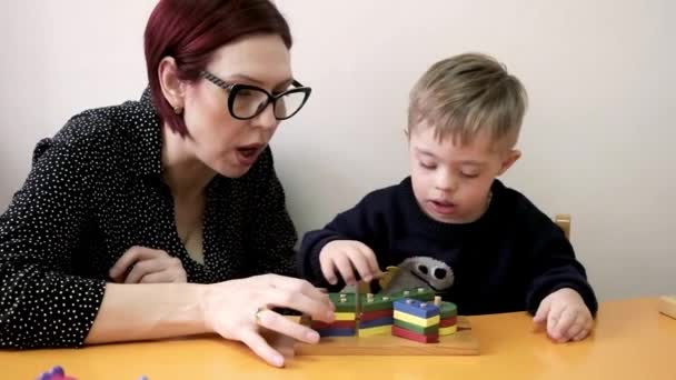 ダウン症の子供は想像力を使って様々な色の幾何学的形状で遊び家族に支えられ — ストック動画