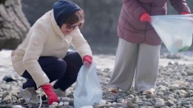 Sorumlu doğa bakımı. Plajda kirlenmiş çevreyi temizleyen plastik çöpleri ve diğer çöpleri toplayan iki genç kadın, ekosistem sorunları