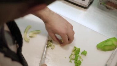 Şefin elleri taze avokadoyu küçük parçalara ayırıyor. Mutfaktaki beyaz kesme tahtasına. Profesyonel aşçı organik ürünlerden vejetaryen salatası hazırlıyor.