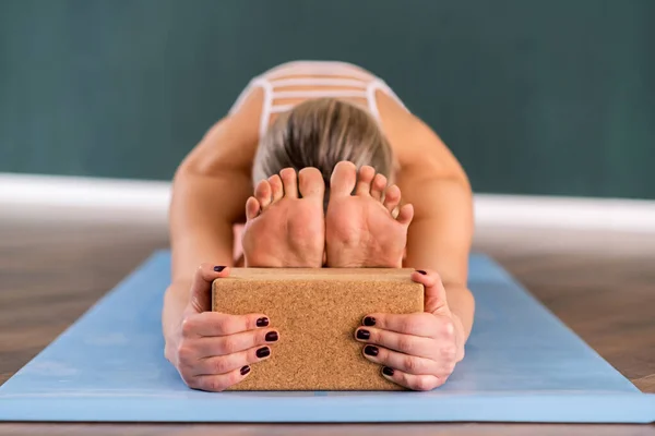 Effective yoga training for body and mind relaxation woman stretching back holding on to block flexible female person doing exercise on blue mat in studio