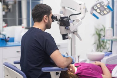 Modern dişçilik kliniğinde kadınların dişlerini detaylarda görebilmek için profesyonel ekipmanlar kullanan dişçiye odaklı dişlerin kontrolü için yenilikçi diş mikroskobu