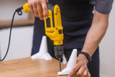 Modern bir dairede elektrikli tornavidayla bacakları ahşap bir askıya bağlayan yetenekli mobilya derleyicisinin ellerini kapat. 