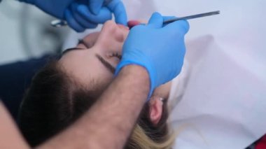 Profesyonel dişçi, kadın hasta görünümlü kadının dişlerini tedavi ediyor. Sandalyeye uzanmış, modern klinikte diş hekimliği hizmetleri yenilikçi ekipmanlar alıyor.