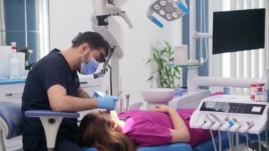 Modern klinikteki dişçi muayenesi. Lastik eldivenli dişçi. Kanepede uzanmış dişlerini tedavi eden kadın dişlerini kontrol ediyor.