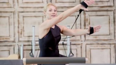 Modern stüdyo profesyonel koçunda etkili pilates dersleri. Spor giyim ve spor kıyafetlerinden hoşlanan sarışın bir kadının kollarını esnetme egzersizlerini gösteriyor.