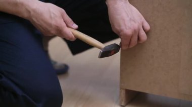 Mobilya üreticisi firma işçisi, ahşap dolaba çivi çakıyor. Odanın içindeki usta tamirci profesyonel aletlerle ahşap işiyle uğraşıyor.