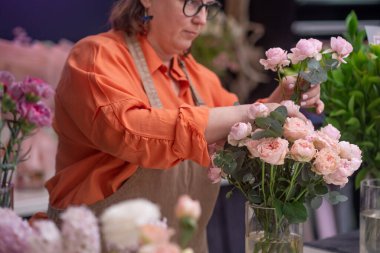 Önlüklü kadın çiçekçi ve işadamı, çiçeklere olan sevgisini ve tasarımı birleştirip göz kamaştırıcı bir buket renkli çiçek açıyor. 