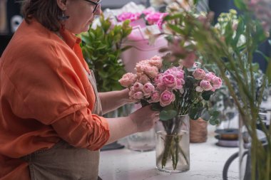 Becerikli elleri ve detaylar için keskin gözleri olan profesyonel bayan çiçekçi, şaşırtıcı bir buket karışık çiçek düzenler.