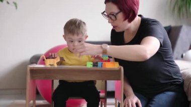  Down sendromlu bir çocuk, yaratıcılıklarını ve öğrenmelerini renkli geometrik şekillerle keşfediyor, aileleri tarafından destekleniyor ve evde rahat ve keyifli bir aktivite yürütüyorlar.