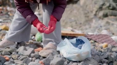 Dünya Günü, yakın planda bir plajda çöp toplayan bir gönüllü tarafından örnek gösteriliyor. Bu eylem sayesinde, bu birey doğal çevrenin korunmasına katkıda bulunuyor..