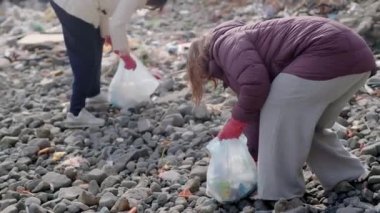 Gönüllüler, kirliliğin azaltılması ve doğal ortamların korunmasına katkıda bulunarak, plastik çöpleri toplayarak kirli bir plajı temizliyorlar.