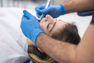 Çağdaş klinikte sandalye kalitesinde dişçilik hizmetlerinde yatan kadın hastaların dişlerini kontrol etmek için tek kullanımlık eldivenler kullanan profesyonel dişçi.