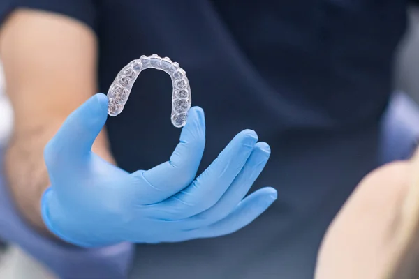 Orthodontist in rubber gloves holding transparent aligners for correction of dentition for patient closeup of innovative caps for teeth alignment in modern dentistry clinic