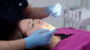 Modern diş hekimliği kliniğinde diş hekiminin elinde dişçi aletleri var. Kadın hastaların dişleri sandalyede uzanıp diş hijyeniyle ilgileniyorlar.
