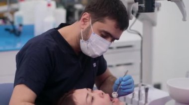 Eldivenli doktorların elinde diş aletleri olan kadın hastaların dişlerini tedavi etmeye hazır ve klinikte profesyonel hizmet sunan ağzı açık bir uzmanla birlikte.