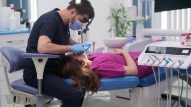 Diş hekimliği kliniği, kanepeye odaklanmış tıbbi maskeli dişçi ve lastik eldiven takan dişçi ve diş aletleriyle dişlerini kontrol eden kadın hastalara detaylı bir muayene uyguladı.