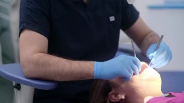 Klinikteki tek kullanımlık eldivenlerle profesyonel diş hekimliği hizmetleri, kadın hasta diş tedavisi için steril diş aletini yakından tutuyor.
