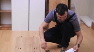 Ev işleri için özel mobilya hizmetleri. Tulum giymiş marangoz, talimatları okuyor. Küçük çiviler ve dairenin zemininde raf tutucuların yanında oturuyor.