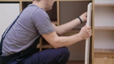 Beyaz kapıyı ahşap dolap uzmanına bağlayan müşteri becerisi olan bir adamın evindeki mobilya montajı profesyonel üniforma üzerine özel prefabrik mobilyalarla çalışır.