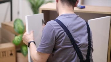 Özel mobilya teslimatı ve montaj ustası oda marangozluğu endüstrisinde ahşap kapıyla çalışan bir müşteri uzmanının evindeki ahşap dolaba beyaz kapı takıyor.