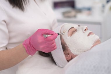 Cilt bakımı uzmanı, cilt sorunları için müşterisine yüz maskesi uyguluyor. Eldivenle ellerini kapat.. 