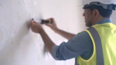 Korumalı miğfer takmış, duvarları ölçen, beyaz bantlı, becerikli işçiler boş bir odada duruyor. Dairenin içini yeniliyor.