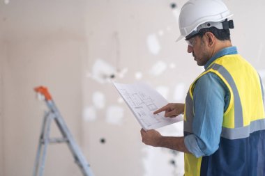 Proje planına işaret eden üniformalı mimar, yenilenme süreci güvenlik kavramı ve ekipmanı oluşturmaya başlamadan önce tamamlanmamış ofis uzmanının önermesini inceliyor.