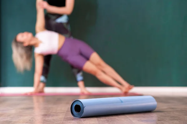 stock image Gymnastic mat roll put on wooden floor against coach helping female student do exercise woman enjoying professional yoga training with specialist in studio