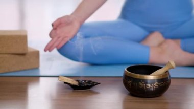 Nilüferli kadın elini mavi hasırlı meditasyonun üzerine koydu. Yanan aroma çubuğu ve hafif yoga stüdyosunda Tibet müzik kasesi yanında.