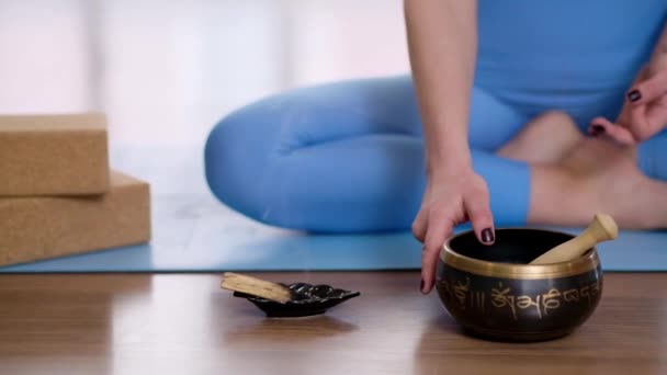 浅色瑜伽演播室里 用站立铃握着藏人歌唱碗 双手插在蓝色垫子上冥想 — 图库视频影像