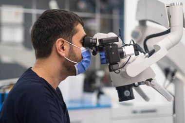 Diş çürüğü muayenesi için profesyonel diş mikroskobu. Modern diş hekimliği kliniğinde dişlerini kontrol eden bir doktor. Yenilikçi teknoloji kullanarak tıbbi maske takıyor.