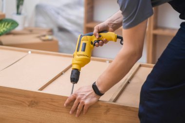 Mobilya montajı, marangoz tulumuyla profesyonel elektrikli marangozluk endüstrisini kullanarak tahta rafa çivi çakıyor.