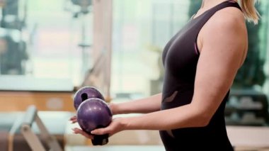 Pilates antrenmanı koçu vücut şekli oluşturmak için spor kıyafetlerinde etkin kas sporcusunu güçlendirmek için halterleri yayarak el ele tutuşuyor.