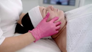 Cilt bakımı uzmanı güzellik kliniğinde gözleri kapalı bir kadına yüz masajı yapıyor.