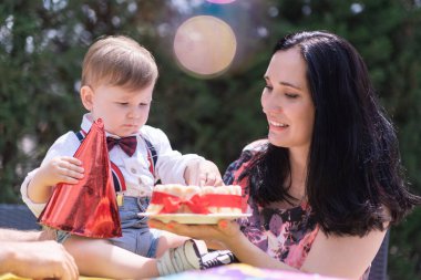 Harika bir ilk doğum günü kutlaması. Bebek çocuk ve annesi ilk yılının dönüm noktasında dışarıda güneşli bir pastayla kutlama yapıyorlar.