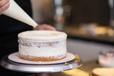 Glütensiz pasta katmanlarını beyaz kremayla kaplayan yemek blogcusu bulanık arka plan kadınının pasta külahını kullanarak şekerlemecilik eğitimi alıyor. Detaylı süreci yakından gösteriyor.