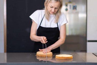 Konsantre şekerlemeci, doğal malzemelerden organik hamur hamuru kesiyor. Siyah önlüklü, sicim bıçaklı kadın, modern mutfaktaki büyük masada duruyor.