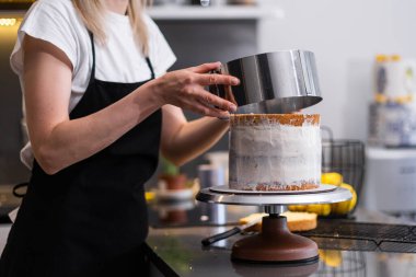Gümüş pasta halkası kullanarak siyah önlüklü, organik kek yapan kadın, adım adım leziz ev yapımı şekerlemeler yapmayı öğretiyor.