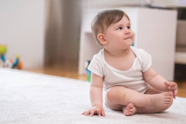 Beyaz elbiseli tombul bir çocuk bebek beşikte çıplak ayakla yere uzanmış, annesinin evde mutlu bir çocukluk geçirmesini ve gelişmesini seyrediyor.