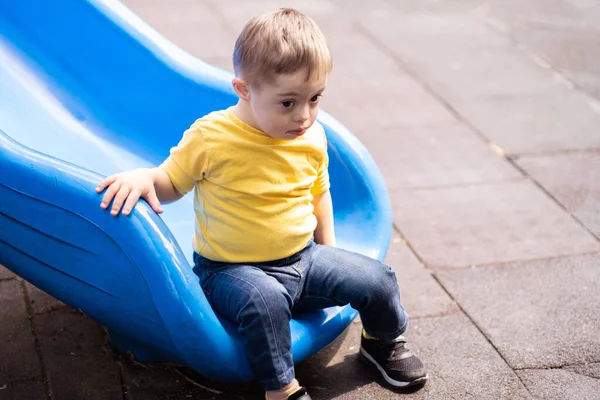 Lindo Niño Pequeño Con Síndrome Sentado Tobogán Azul Patio Recreo —  Fotos de Stock