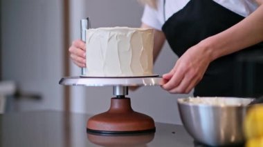 Siyah önlüklü ev hanımı düğün kutlaması için beyaz mastikle enfes pastalar yapıyor. Kadın modern mutfakta organik ev yapımı şekerlemeler hazırlıyor.