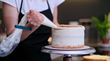 Tatmin olmuş sarışın kadın pastaya organik malzemelerden yapılmış lezzetli bir krema koymak için pasta külahı kullanıyor siyah önlüklü ev hanımı evde el yapımı şekerlemeler yapıyor.