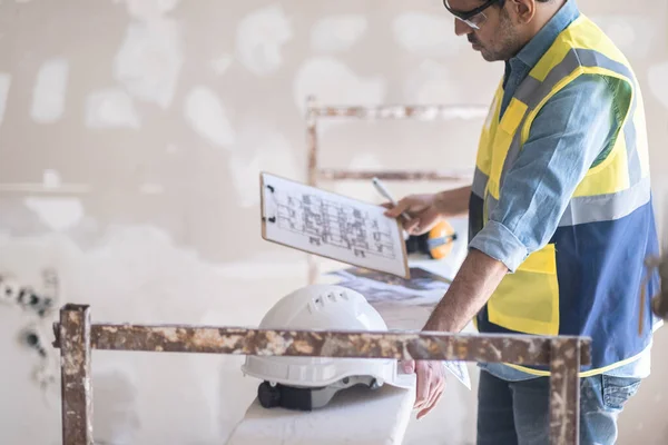 stock image Focused architect in glasses holding clipboard with apartment drawing blueprint in hand specialist checking project plan before starting renovation process in room