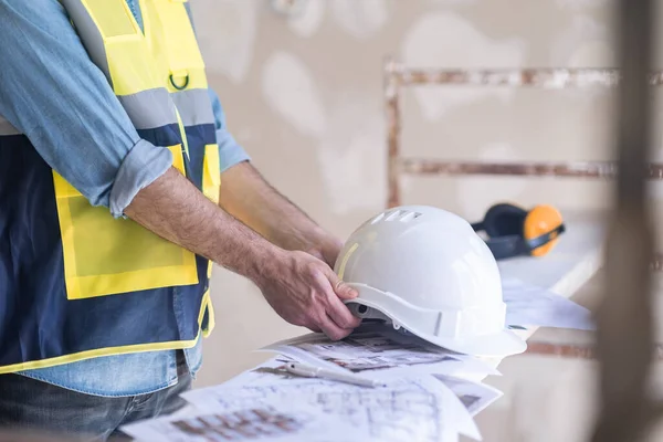 stock image Engineer taking white protective hardhat before processing shabby wall in premise construction safety equipment and heap of project papers renovation process in office