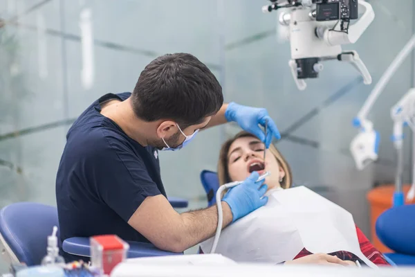 Professional dental checkup of female patient in modern dentistry clinic doctor looking at teeth of young woman on dentist chair using mirror and professional tools